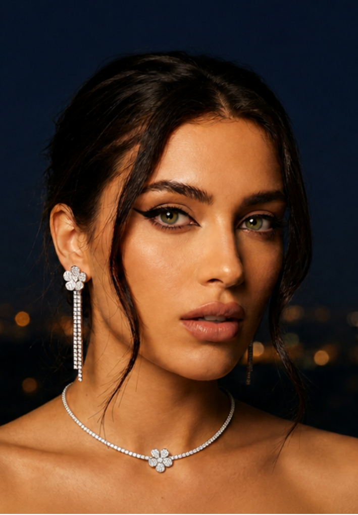 A close-up portrait of a woman wearing a matching floral diamond necklace and matching long drop earrings against a dark, softly blurred cityscape background.