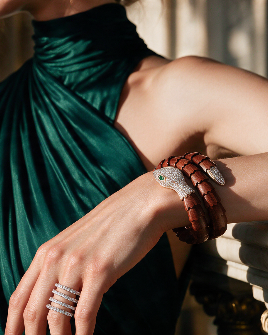 A close-up lifestyle shot of a model wearing a sculptural snake bracelet with a brown leather body and a silver diamond-encrusted head, paired with diamond rings and a dark green draped dress.